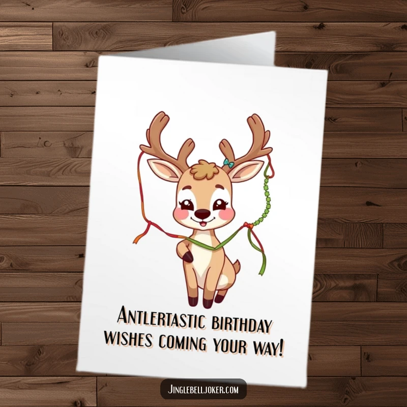 Funny Free Printable Birthday Card: A deer joker with festive antlers playfully bats at a dangling tinsel strand.